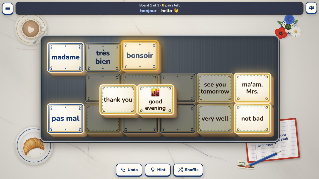 Board 1 part played on a dark zinc tray on a marble café table. French words sit on tiles with blue frames and English meanings on tiles with yellow frames. Bonsoir is picked up with a gold rim, its partner good evening is bright and free in the middle, the tiles in the shade (très bien, see you tomorrow, very well) are blocked, and the status bar shows the last pair taken: bonjour · hello, with a waving hand.